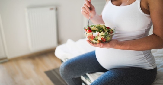 pregnant woman holding a bowl of salad and fork