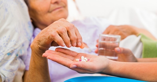 older woman taking medication from a nurse