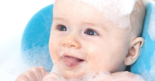 infant sitting in a baby bath covered in bubbles