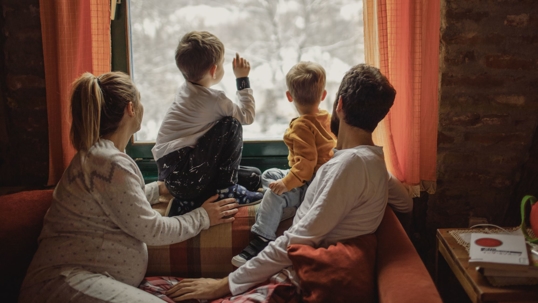 family with small children watching snow outside window